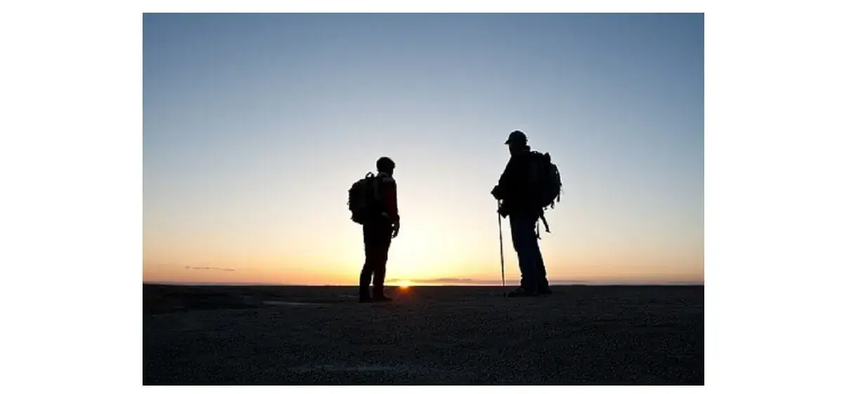 モンベルのトレッキングポールをもって朝日の中を登山をしている登山者2人