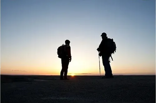 モンベルのトレッキングポールをもって朝日の中を登山をしている登山者2人 